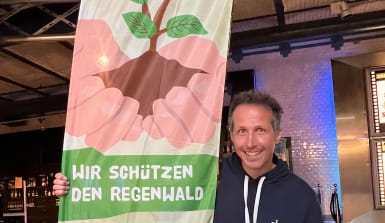 Willi Weitzel steht lachend vor einem Abenteuer Regenwald Banner