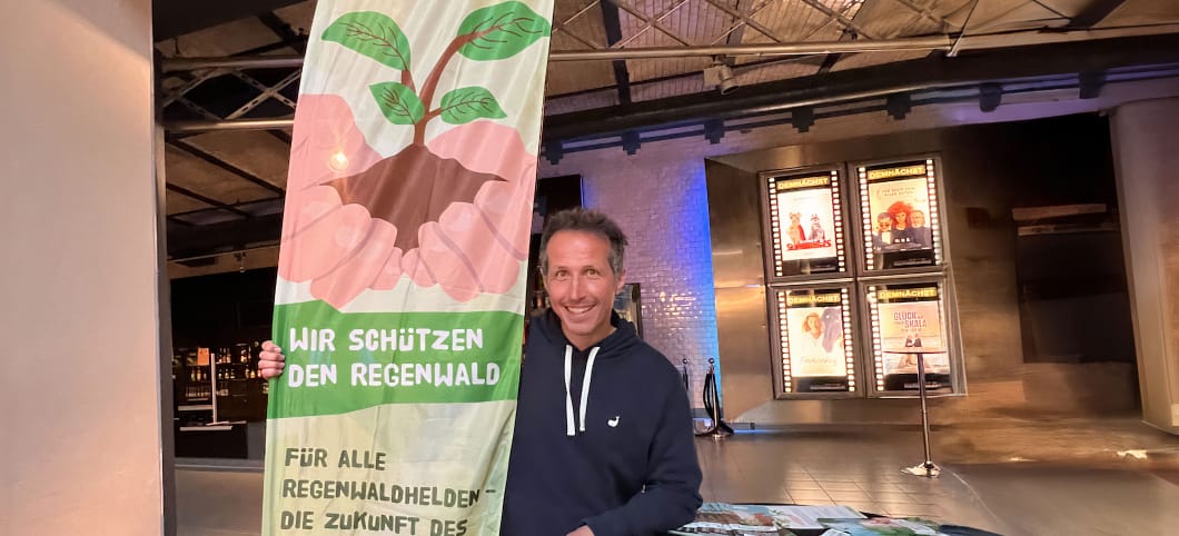 Willi Weitzel steht lachend vor einem Abenteuer Regenwald Banner